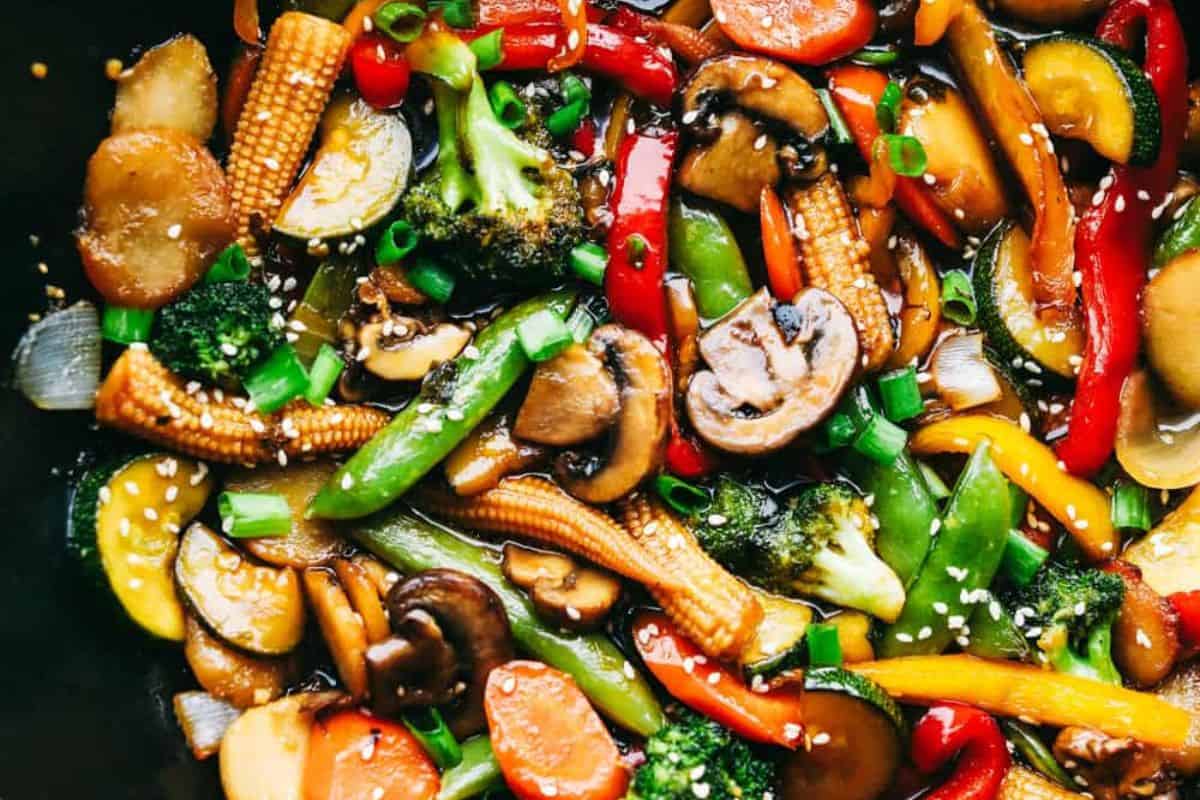 Colorful vegetable stir-fry with mushrooms, broccoli, baby corn, bell peppers, snap peas, zucchini, carrots, and green onions in a savory sauce—perfect for Lent or anyone seeking delicious meatless meals. Finished with a sprinkle of sesame seeds.