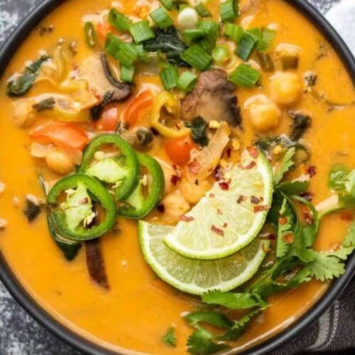 A bowl of creamy orange soup, perfect for Lent recipes, topped with lime slices, jalapeño, cilantro, green onions, and visible vegetables and beans.