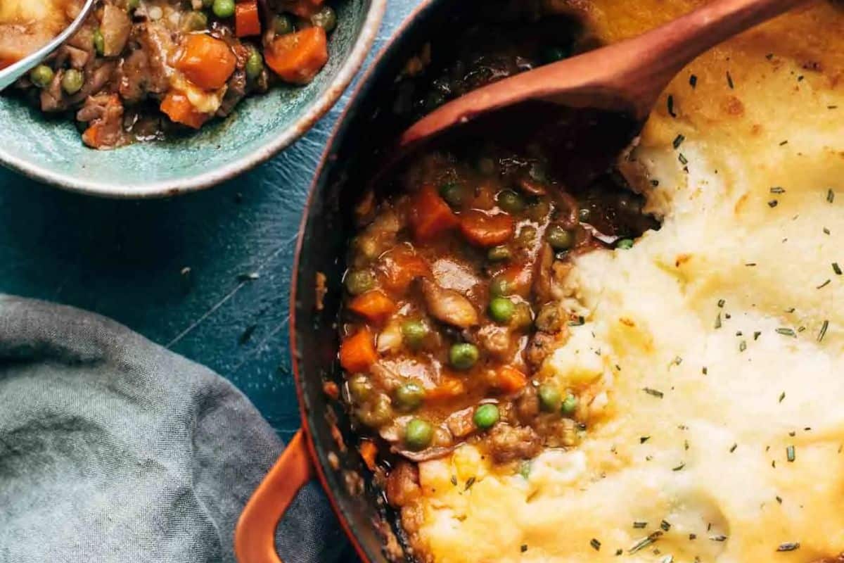 A close-up of a casserole dish with shepherd’s pie, featuring creamy mashed potatoes on top and a filling of peas and carrots, perfect for Lent recipes, with a serving scooped into a bowl beside it.