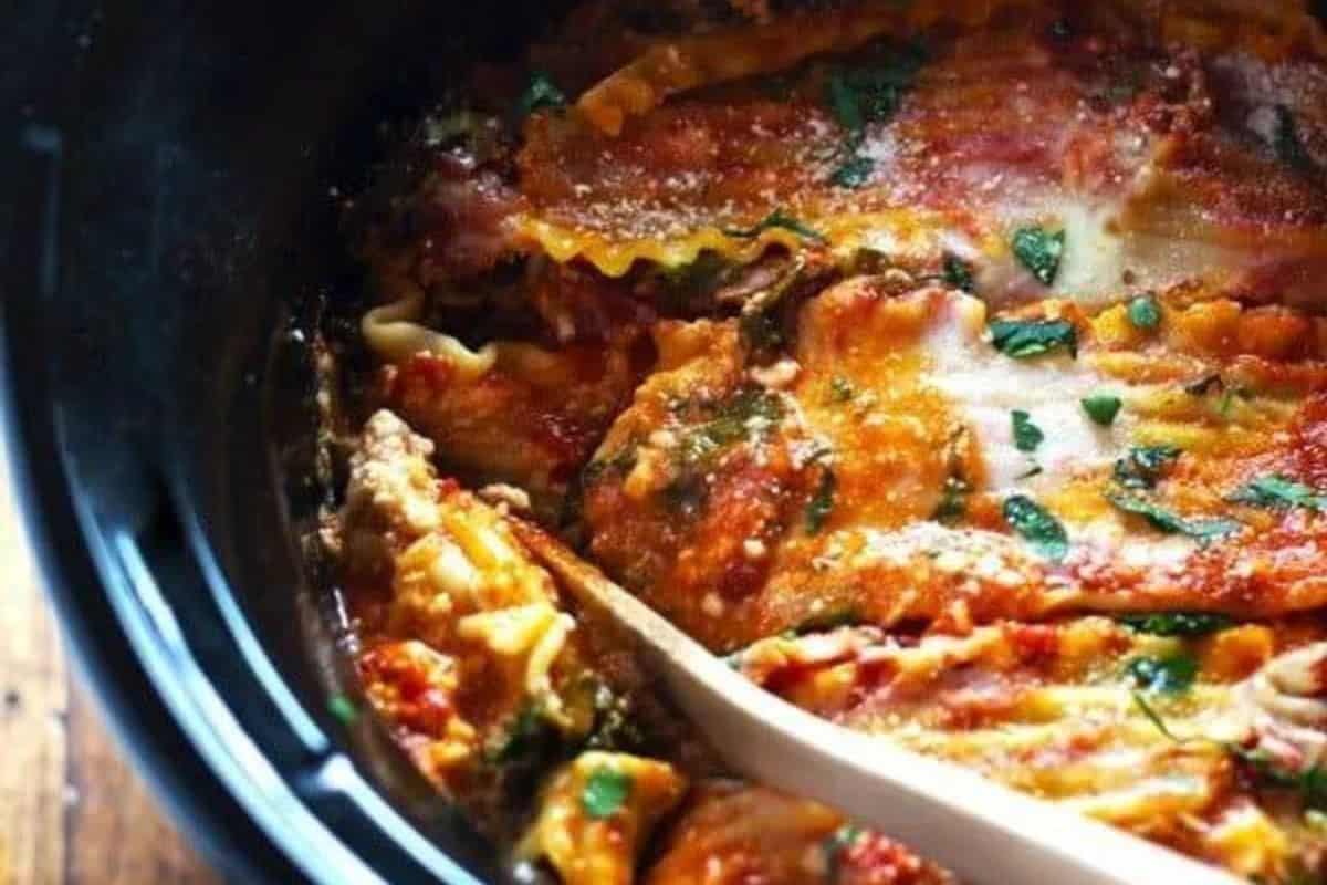 Close-up of lasagna with sauce and herbs in a slow cooker, perfect for meatless recipes during Lent, with a wooden spoon partially visible on the side.