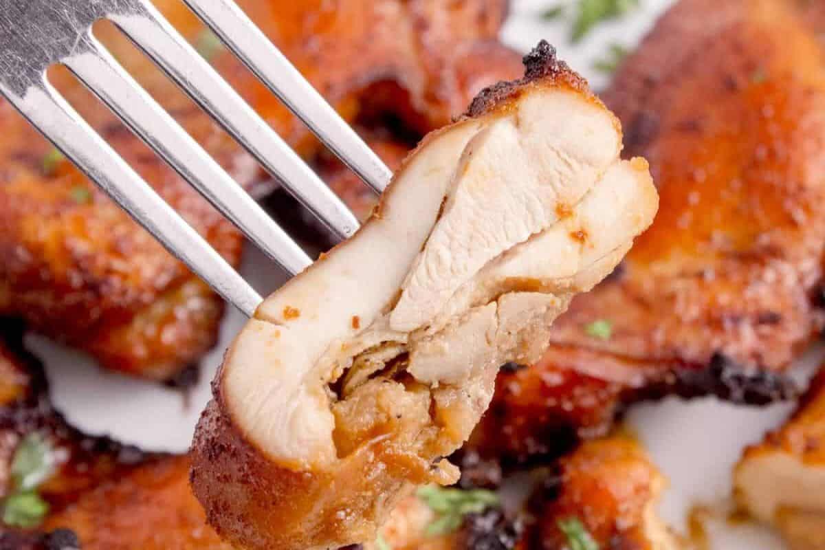 A fork holds a piece of cooked, seasoned chicken with a browned, slightly charred exterior and moist interior—perfect for trying out new chicken thigh recipes.