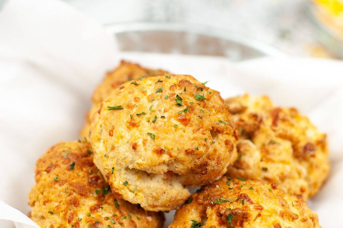 A plate of golden-brown cheddar biscuits, crafted with restaurant-inspired recipes and garnished with herbs, sits invitingly on a white napkin.
