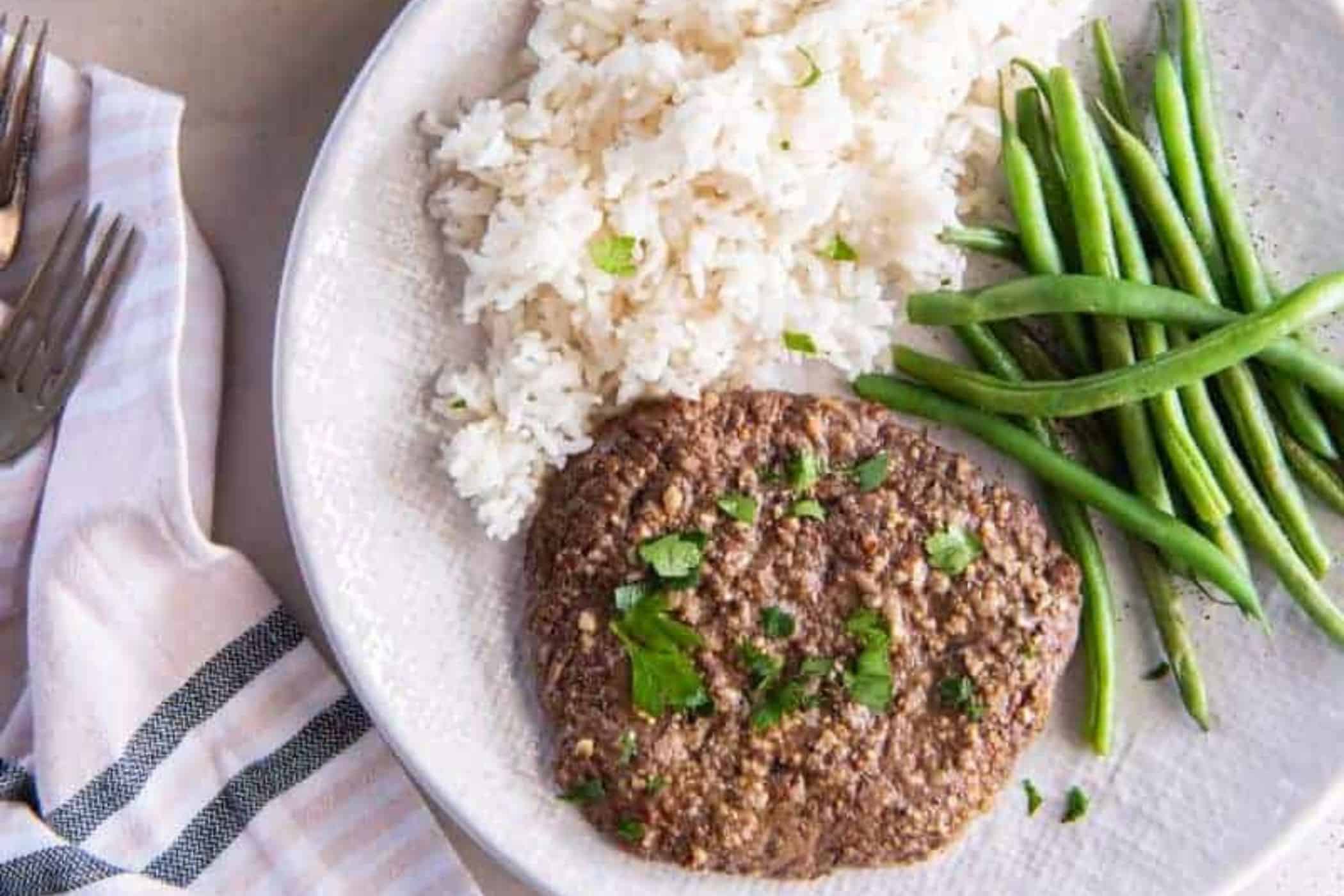 A plate with white rice, green beans, and a seasoned air fried cube steak garnished with fresh herbs—perfect for busy weeknights or as inspiration for easy cube steak recipes.
