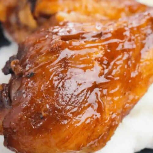 Close-up of a glazed, roasted chicken drumstick—an irresistible choice for finger licking chicken—served on a bed of creamy white food, possibly mashed potatoes or grits.