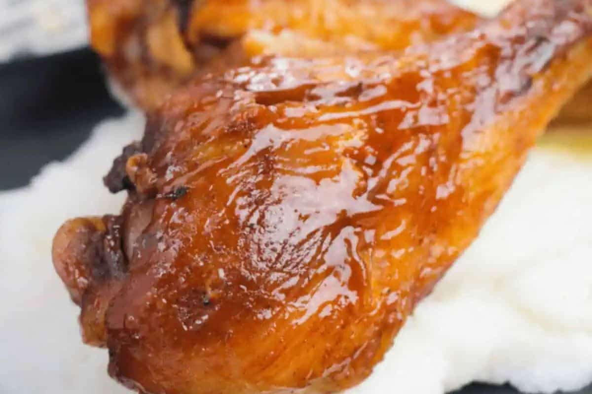 Close-up of a glazed, roasted chicken drumstick—an irresistible choice for finger licking chicken—served on a bed of creamy white food, possibly mashed potatoes or grits.
