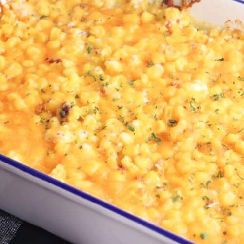 Corn Casserole with Cream Cheese: Baked casserole dish filled with creamy corn and rich cream cheese, topped with melted cheese and herbs, resting on a black and white cloth.