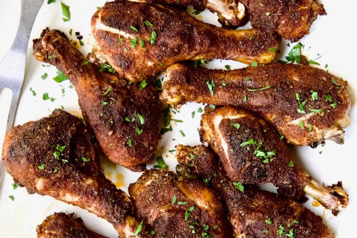 Several cooked and seasoned chicken drumsticks, perfect for Finger Licking Chicken lovers, are garnished with chopped parsley and arranged on a white surface.