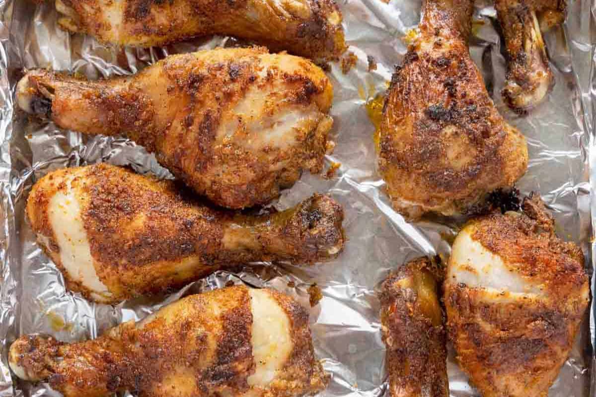 Eight seasoned and baked chicken drumsticks arranged on a foil-lined baking sheet—an irresistible choice for anyone who loves Finger Licking Chicken.