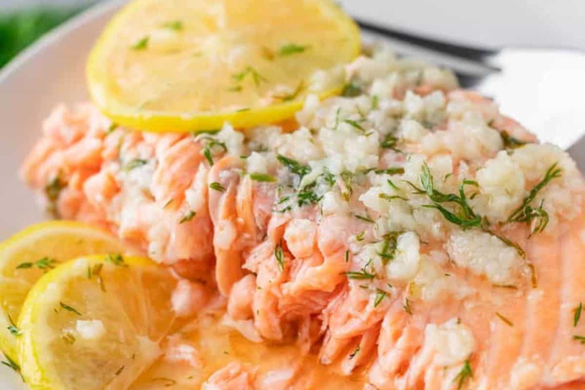  A close-up of a piece of baked salmon, garnished with lemon slices and a creamy white sauce.