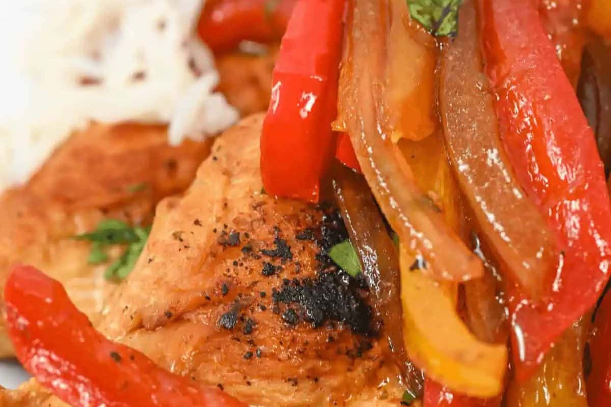 Close-up of cooked chicken with char marks, topped with sliced red and yellow bell peppers and onions, served next to white rice garnished with herbs—an easy dinner idea that's simply delicious.
