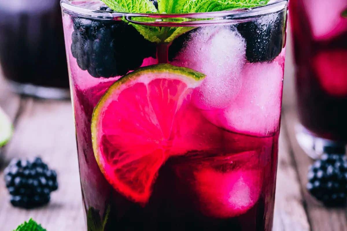 A glass of iced blackberry drink garnished with lime slices and mint leaves, with visible blackberries and ice cubes—a refreshing sip inspired by classic cocktails.