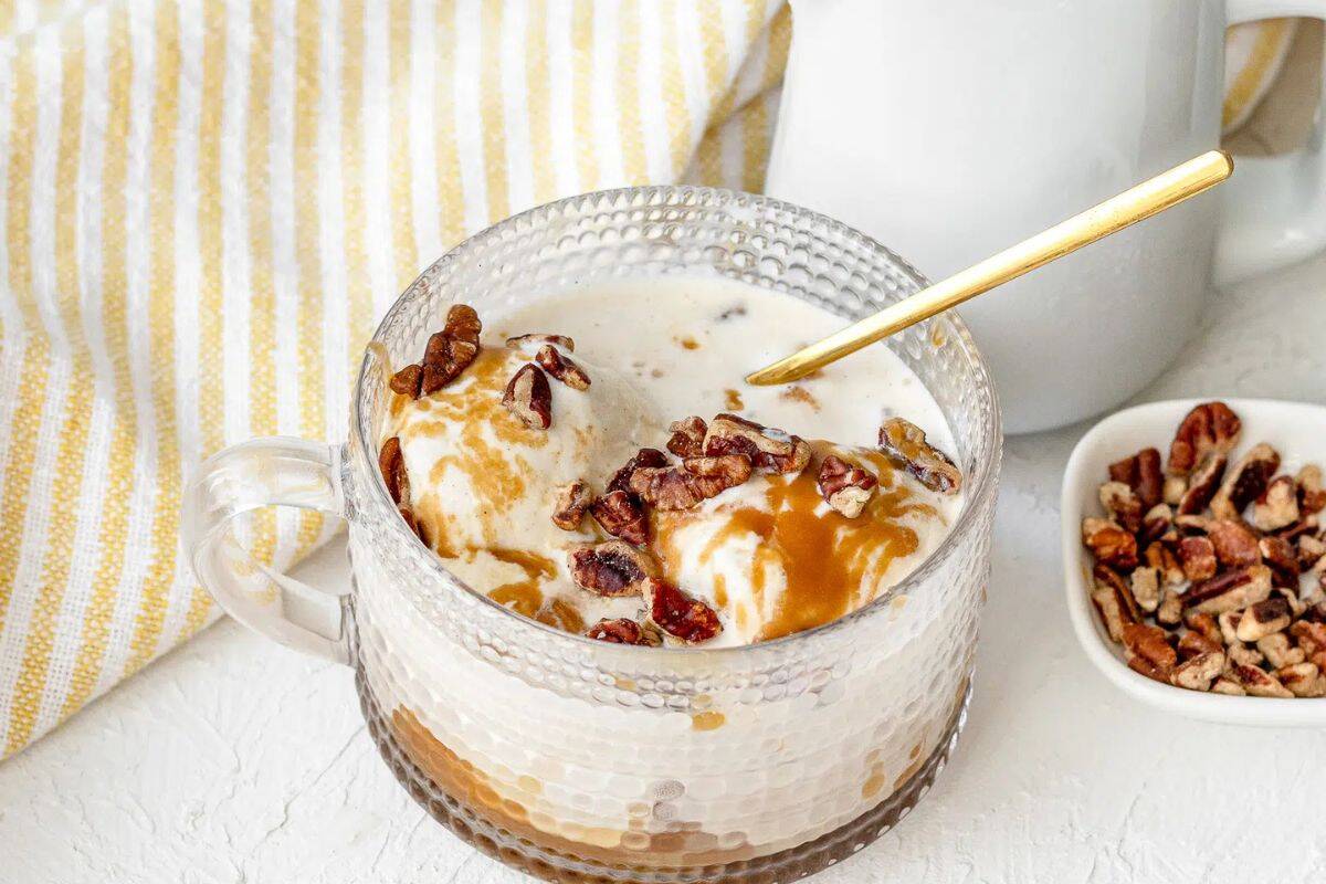 A glass cup filled with ice cream topped with easy caramel sauce and pecans, with a gold spoon, next to a small dish of pecans and a striped cloth—perfect for fans of indulgent desserts.