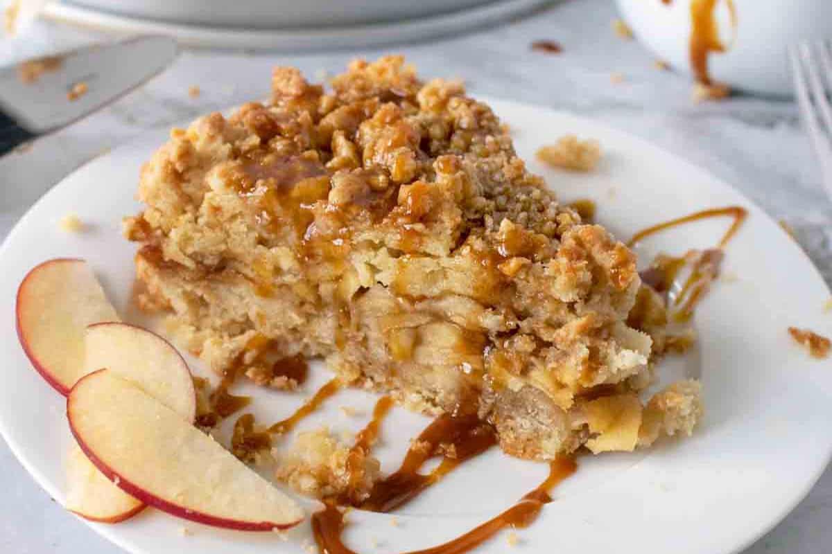 A slice of caramel apple torte with an easy caramel drizzle on a white plate, garnished with apple slices—perfect for fans of indulgent desserts.