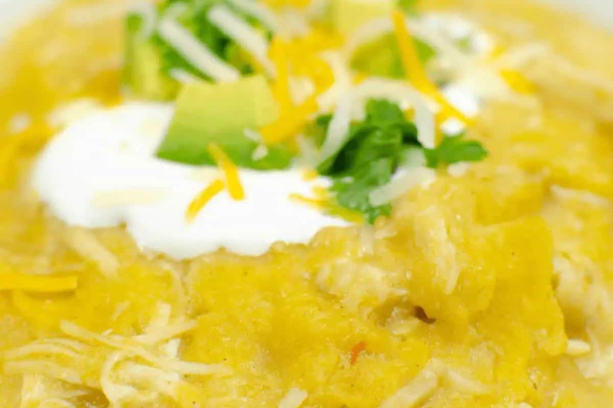 Close-up of a bowl of creamy chicken enchilada casserole topped with sour cream, shredded cheese, avocado chunks, and chopped cilantro—an easy Instant Pot recipe that’s sure to become a game changer for cozy meals.