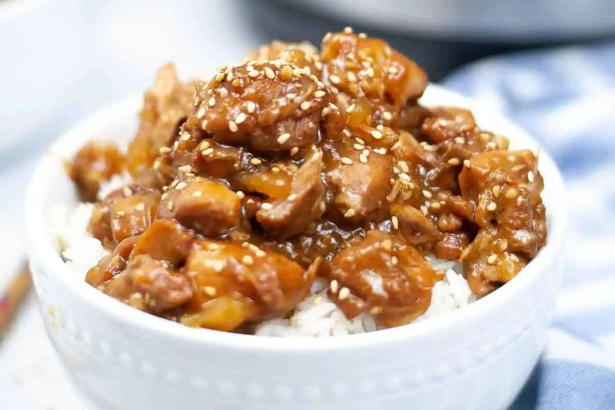 A bowl of white rice topped with glazed chicken pieces and sprinkled with sesame seeds—a game changing dish you’ll want to repeat. Perfect for fans of Instant Pot recipes!.