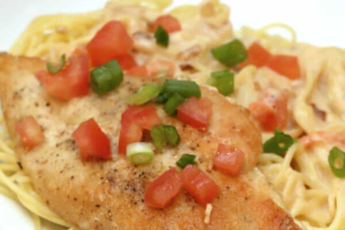 Savor this restaurant-inspired recipe: Grilled chicken breast topped with diced tomatoes and green onions, all on a bed of creamy pasta. Perfect to make at home for a delightful dinner experience.