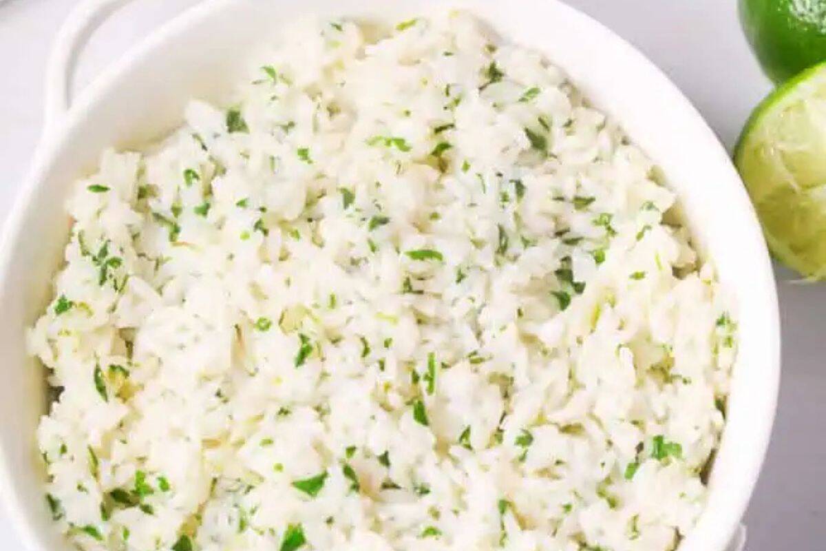 A bowl of white rice mixed with chopped cilantro, placed next to a halved lime, offers a fresh and zesty twist to a classic dish. Perfect for those seeking restaurant inspired recipes to make at home.