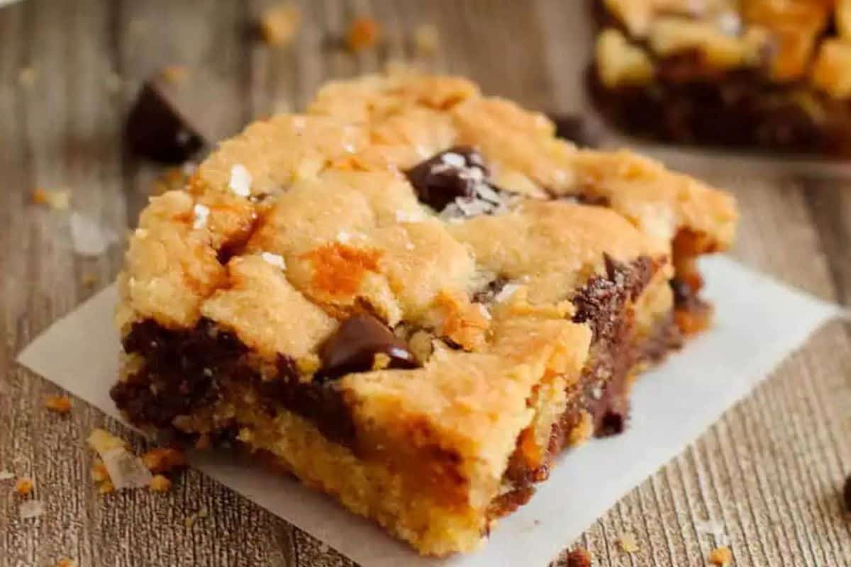 A close-up of a chocolate chip caramel blondie bar on parchment paper, resting on a wooden surface—perfect for fans of indulgent desserts and those seeking easy caramel inspiration.