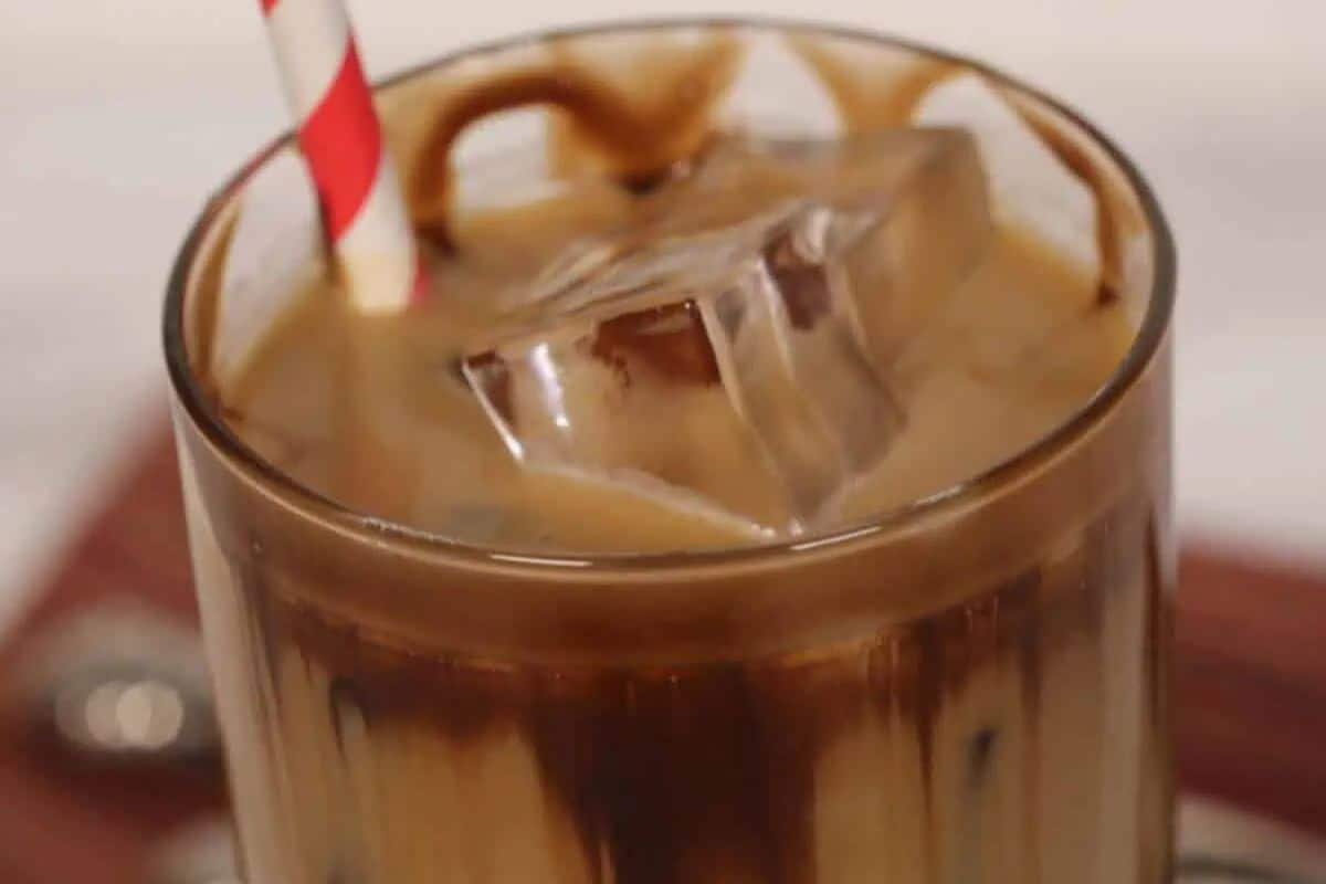 A glass of iced coffee with swirls of chocolate and caramel syrup, a red and white striped straw, and ice cubes—perfect for fans of indulgent desserts or easy caramel recipes.