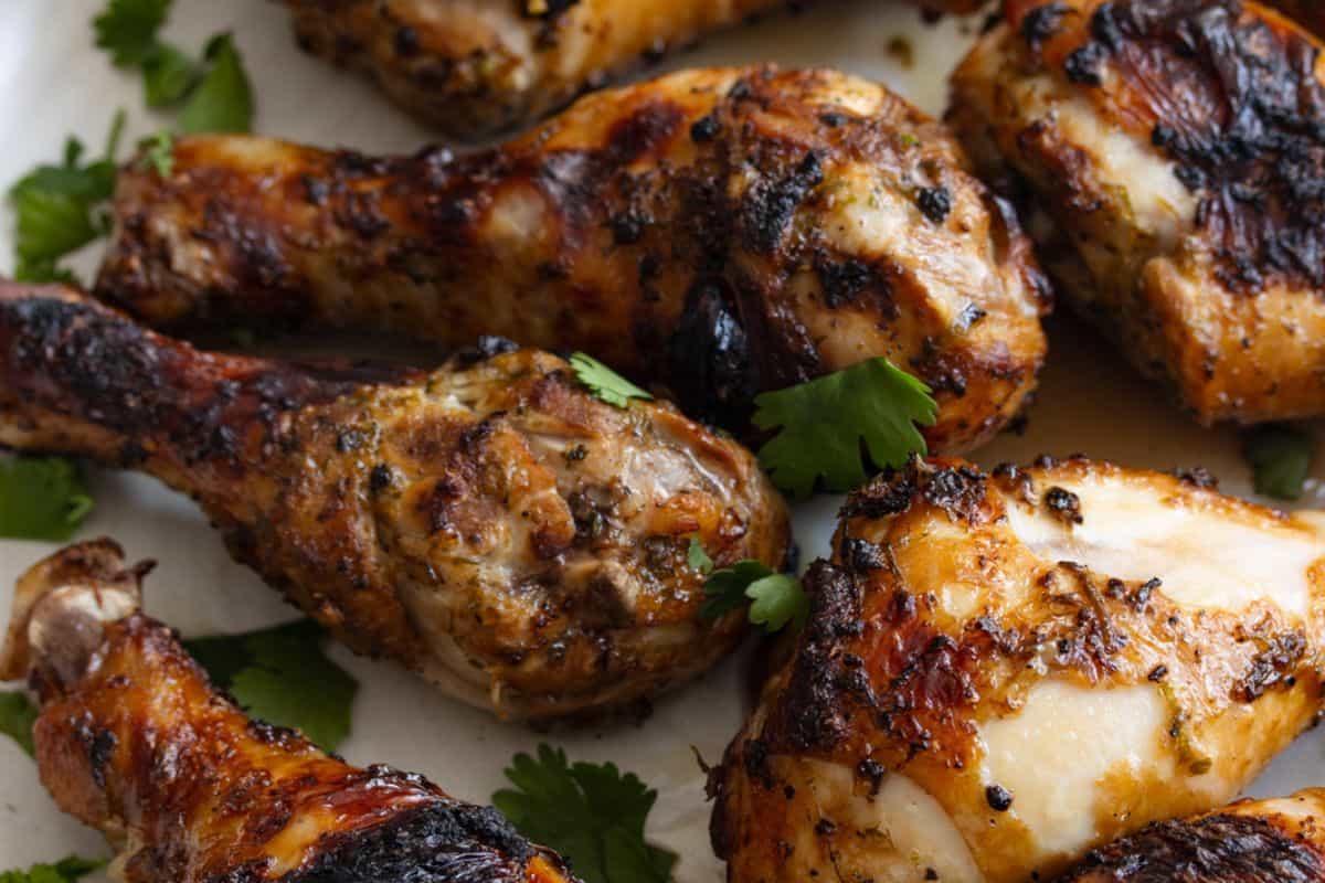 Close-up of several finger licking chicken drumsticks, garnished with fresh cilantro on a white plate—perfect for anyone searching for delicious chicken recipes.
