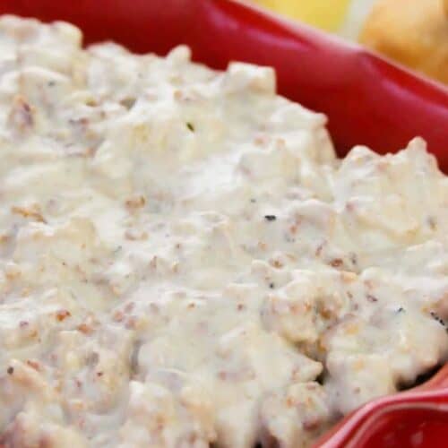A red dish filled with creamy sausage gravy, with pieces of sausage visible; biscuits are partially seen in the background—a nod to classic recipes and timeless meals.