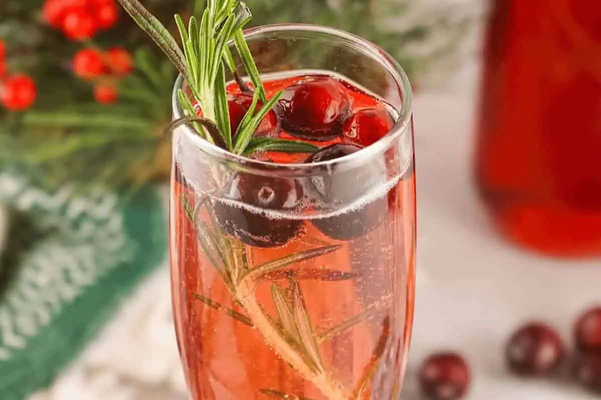 A Cranberry Mimosa featuring cranberry juice, sparkling wine, fresh cranberries, and rosemary.