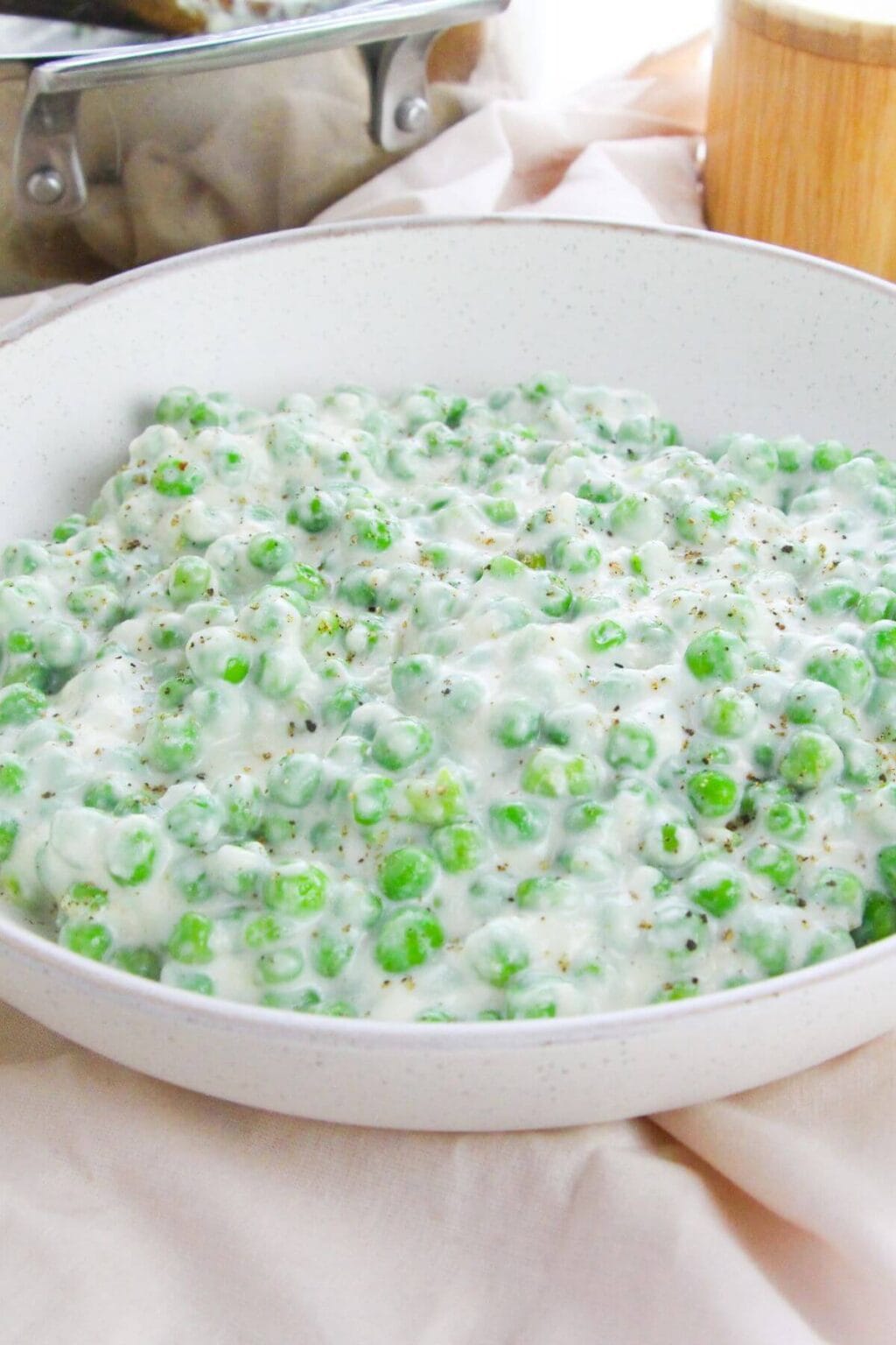 A white bowl filled with creamed peas in a creamy white sauce, placed on a light-colored tablecloth.