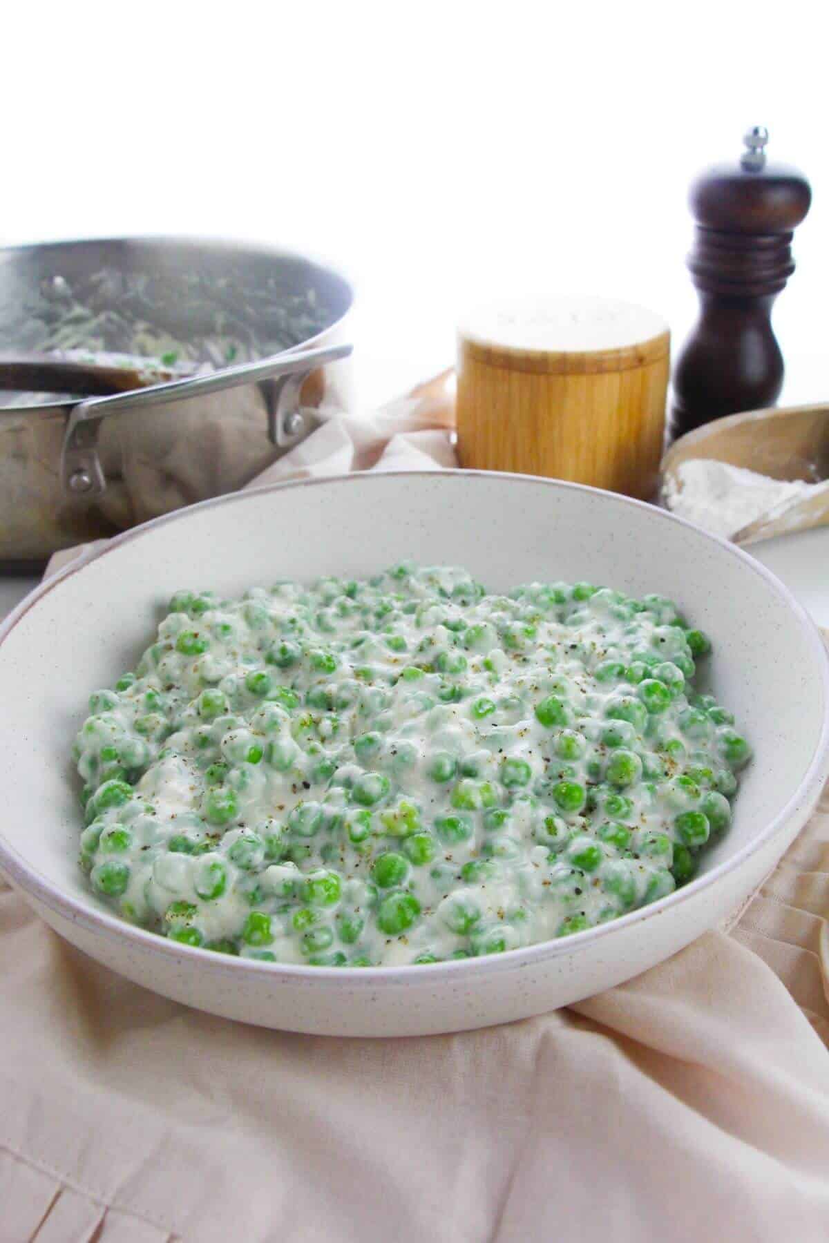 A bowl of side dish sits on a light cloth, with a pan, pepper grinder, and wooden container in the background, highlighting this classic comfort dish.