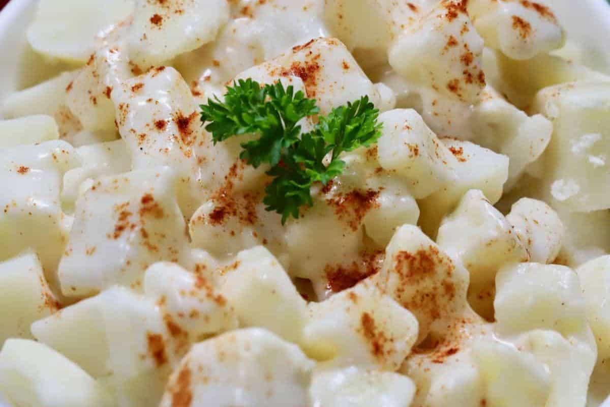 A close-up of creamy potato salad, a staple among classic recipes, topped with paprika and garnished with a sprig of parsley.