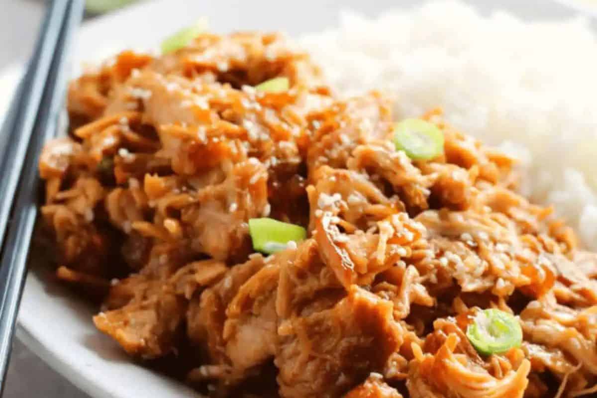 A plate of juicy teriyaki chicken, garnished with chopped green onions and sesame seeds, served alongside white rice. Perfect for fans of Chicken Thigh Recipes. Chopsticks are placed on the side.