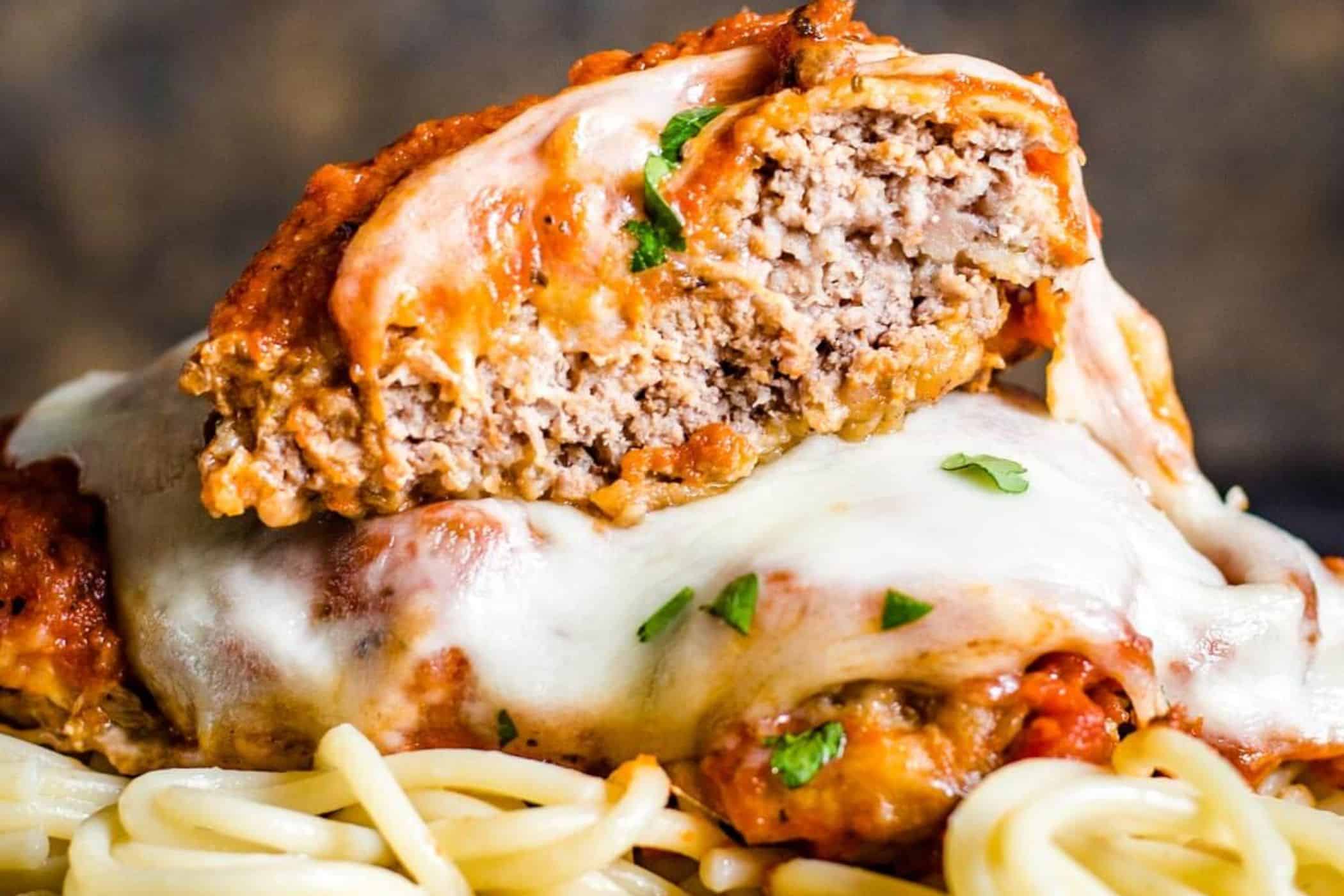 Close-up of cube steak parmesan with melted cheese and tomato sauce, served over spaghetti with parsley garnish—a must try dish perfect for busy weeknights.