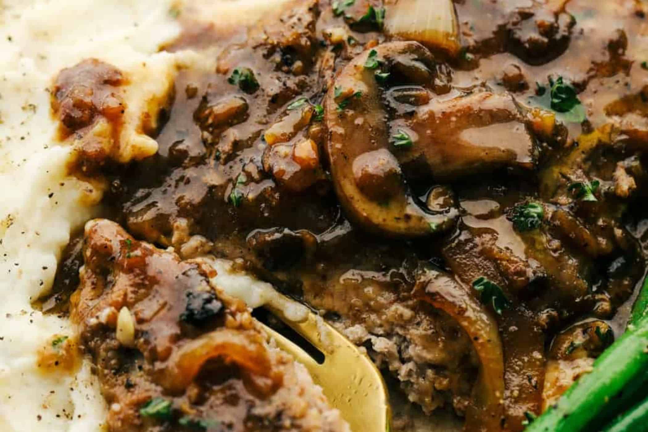 Close-up of cube steak with mushroom gravy—a classic choice for cube steak recipes—topped with brown mushroom and onion gravy, served alongside mashed potatoes. Perfect for busy weeknights.