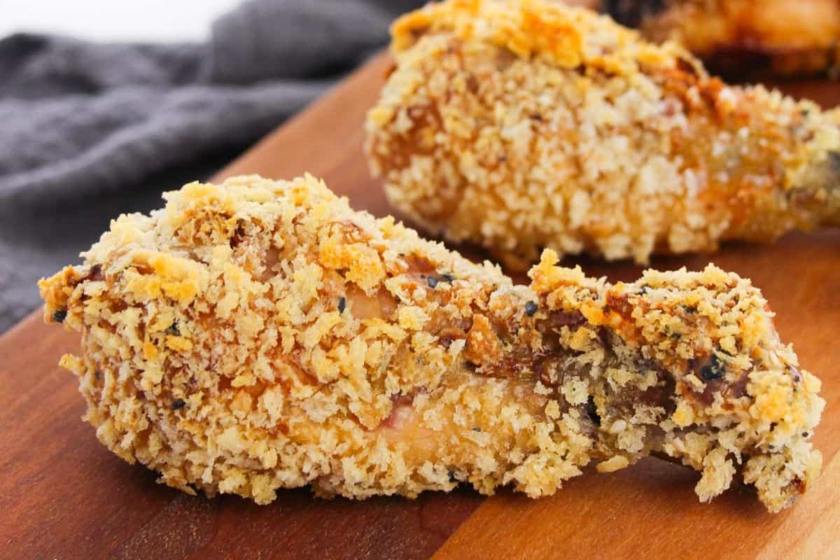 A close-up of a crispy, breaded chicken drumstick on a wooden surface, perfect for fans of finger licking Chicken Drumstick Recipes, with another drumstick blurred in the background.