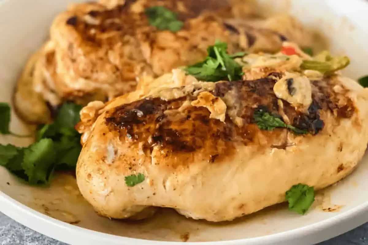 Two pieces of seasoned and cooked chicken breast rest on a white plate, garnished with cilantro and thinly sliced vegetables—perfect as an easy dinner for two.