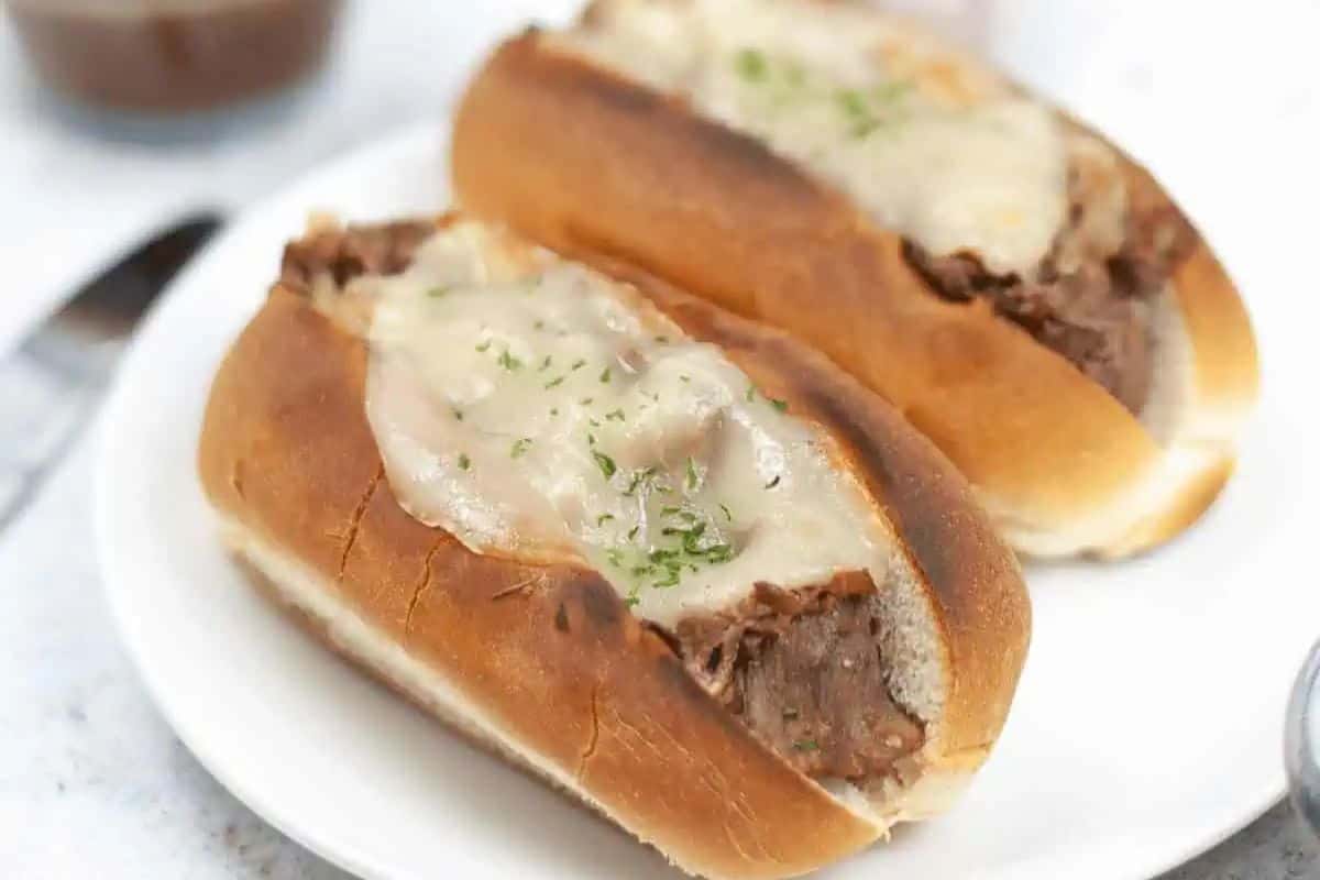 Two beef sandwiches on hoagie rolls topped with melted cheese, served on a white plate—a game changing option for easy meals and perfect for those who love Instant Pot recipes.