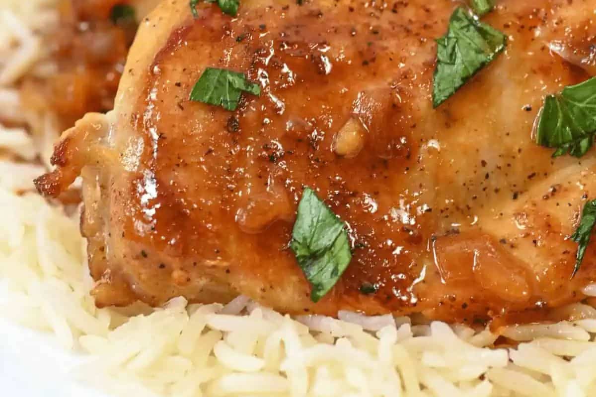 Close-up of a glazed chicken piece garnished with herbs, served on a bed of rice—perfect for a delicious dinner for two.