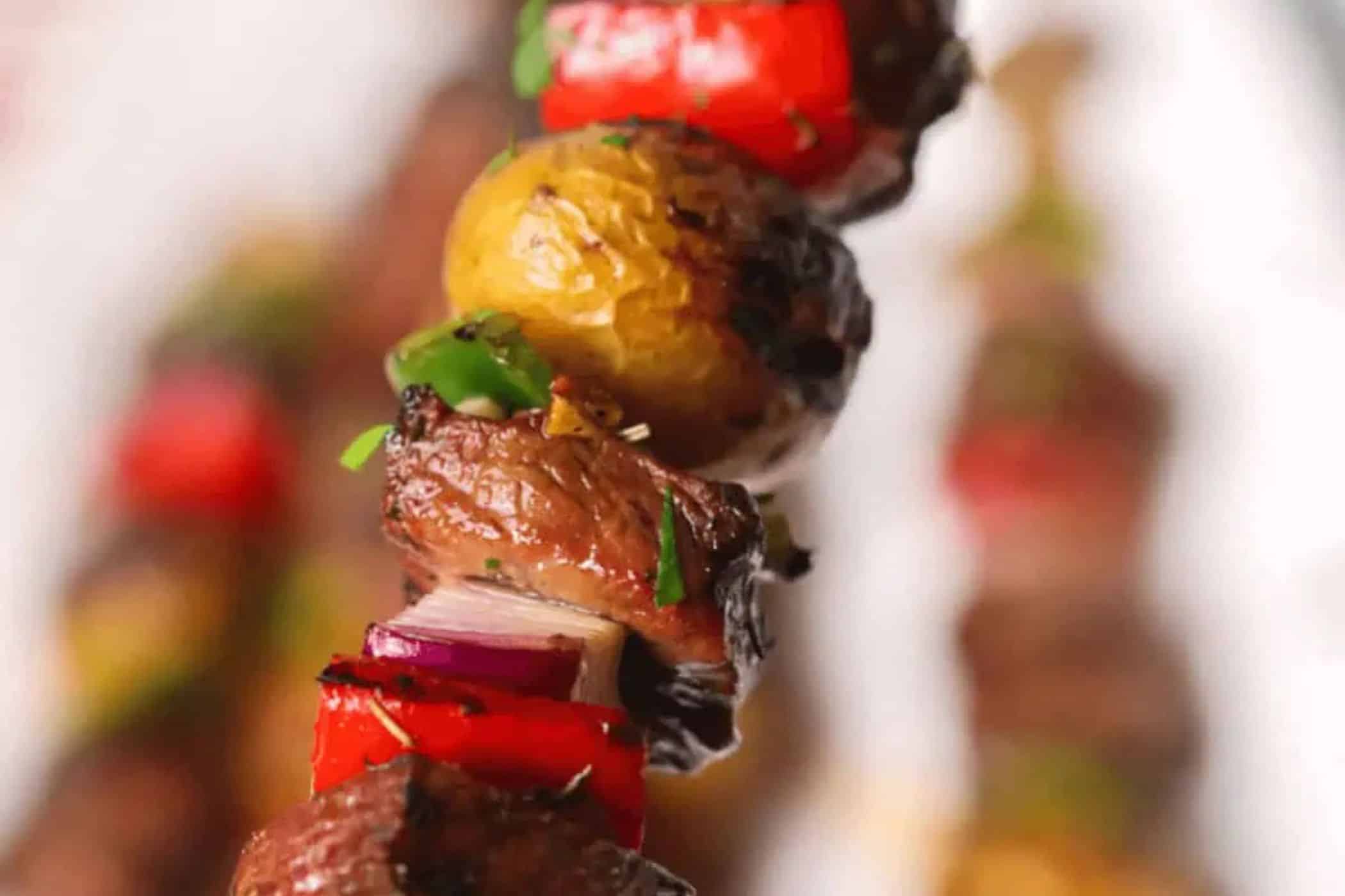 A close-up of a grilled skewer with pieces of beef, red bell pepper, yellow potato, red onion, and chopped herbs—perfect for cube steak recipes on busy weeknights.