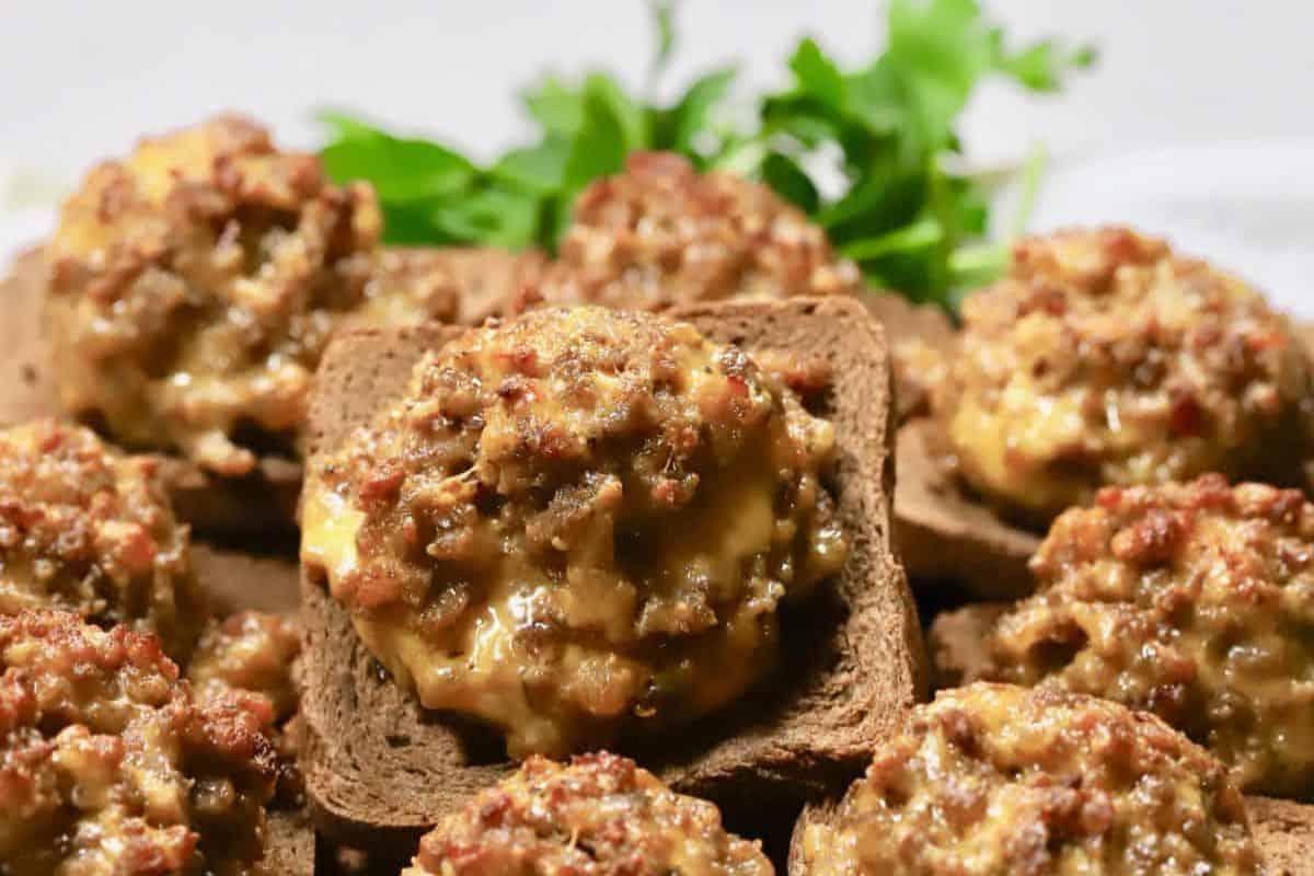 Several pieces of rye bread topped with a baked cheesy sausage mixture, reminiscent of vintage dishes, are garnished with fresh parsley in the background.