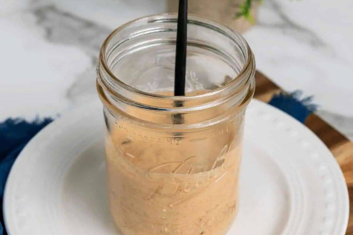 A close-up of a clear glass jar filled with creamy, pale orange-pink Homemade Big Mac Sauce. A black straw is visible in the jar.
