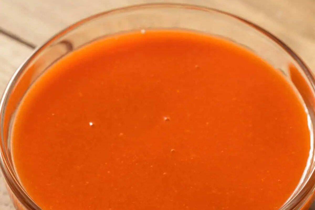 A close-up overhead shot of a clear glass bowl filled with smooth, vibrant orange-red Homemade Chicken Wing Sauce.