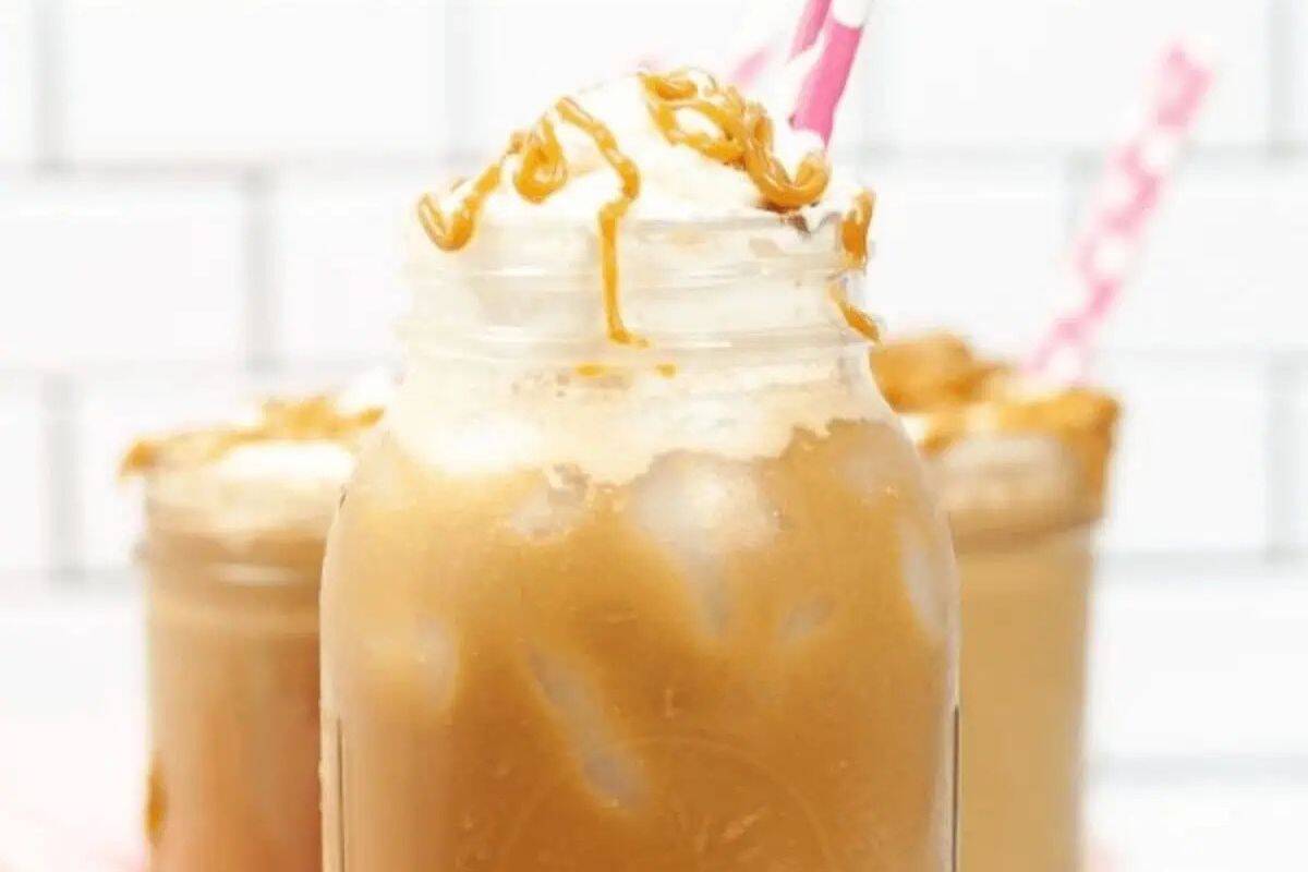 A mason jar filled with iced caramel macchiato, topped with whipped cream and caramel drizzle, with two pink striped straws—a refreshing treat inspired by indulgent desserts and easy caramel delights.