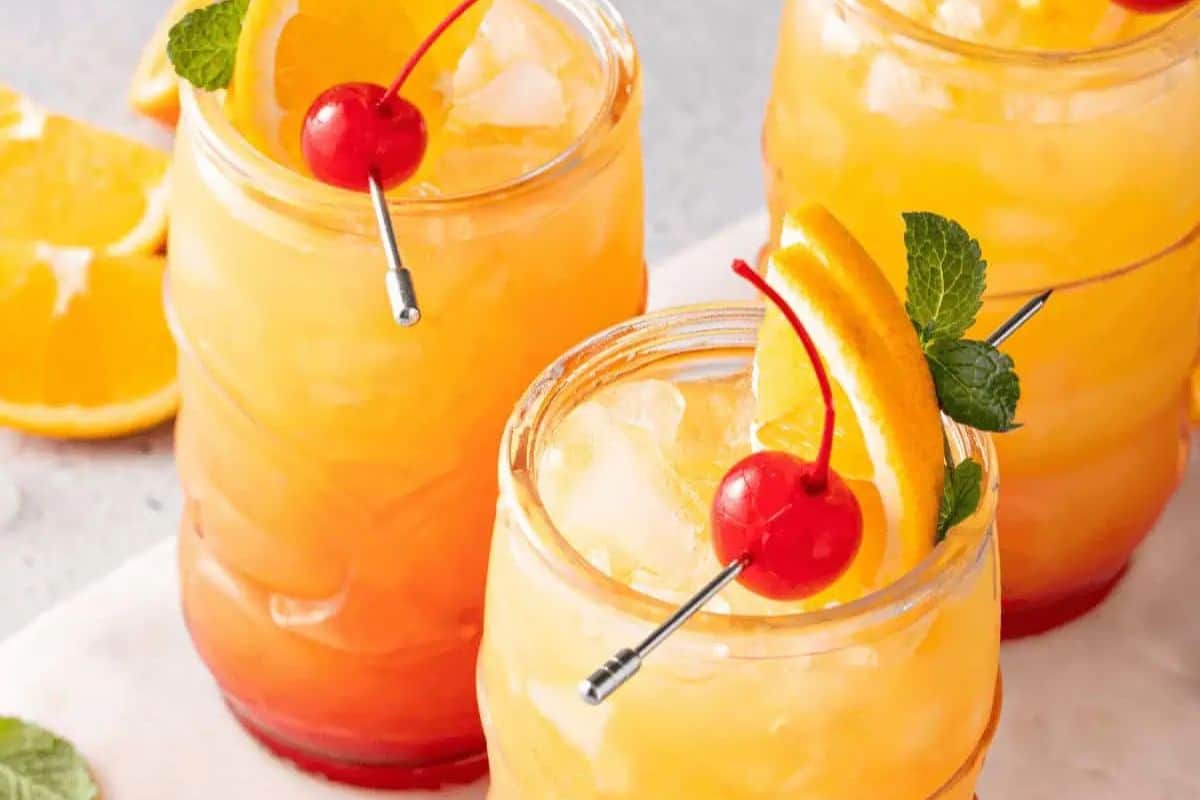 Jamaican Rum Punch featuring rum, orange juice, pineapple juice, grenadine, and garnished with orange, cherry, and mint.