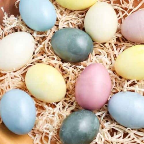 A wooden bowl filled with shredded paper holds a variety of pastel-colored eggs, including blue, yellow, green, white, and pink—perfect for easy Easter crafts or inspiring new Easter egg ideas.