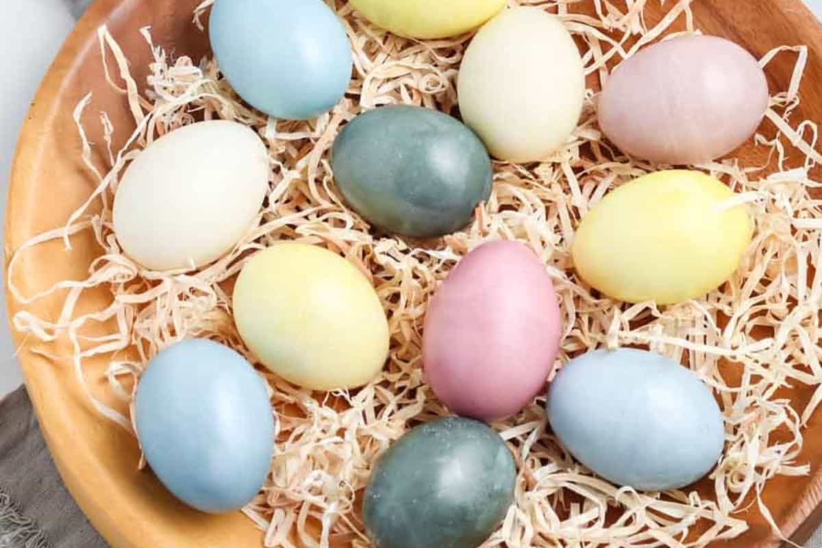A wooden bowl filled with shredded paper holds a variety of pastel-colored eggs, including blue, yellow, green, white, and pink—perfect for easy Easter crafts or inspiring new Easter egg ideas.