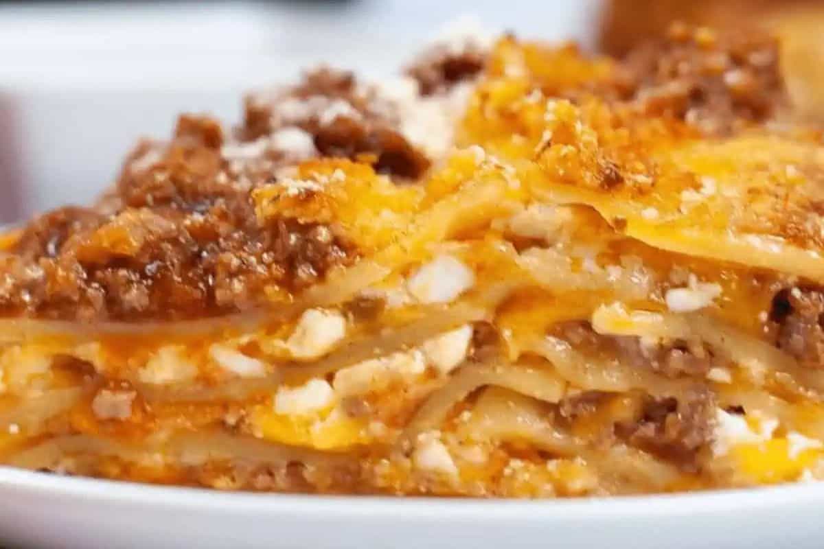 Close-up of a slice of lasagna showing layers of pasta, ground meat, cheese, and sauce on a white plate—this classic dish is one of those easy meals that’s truly game changing for any dinner table.