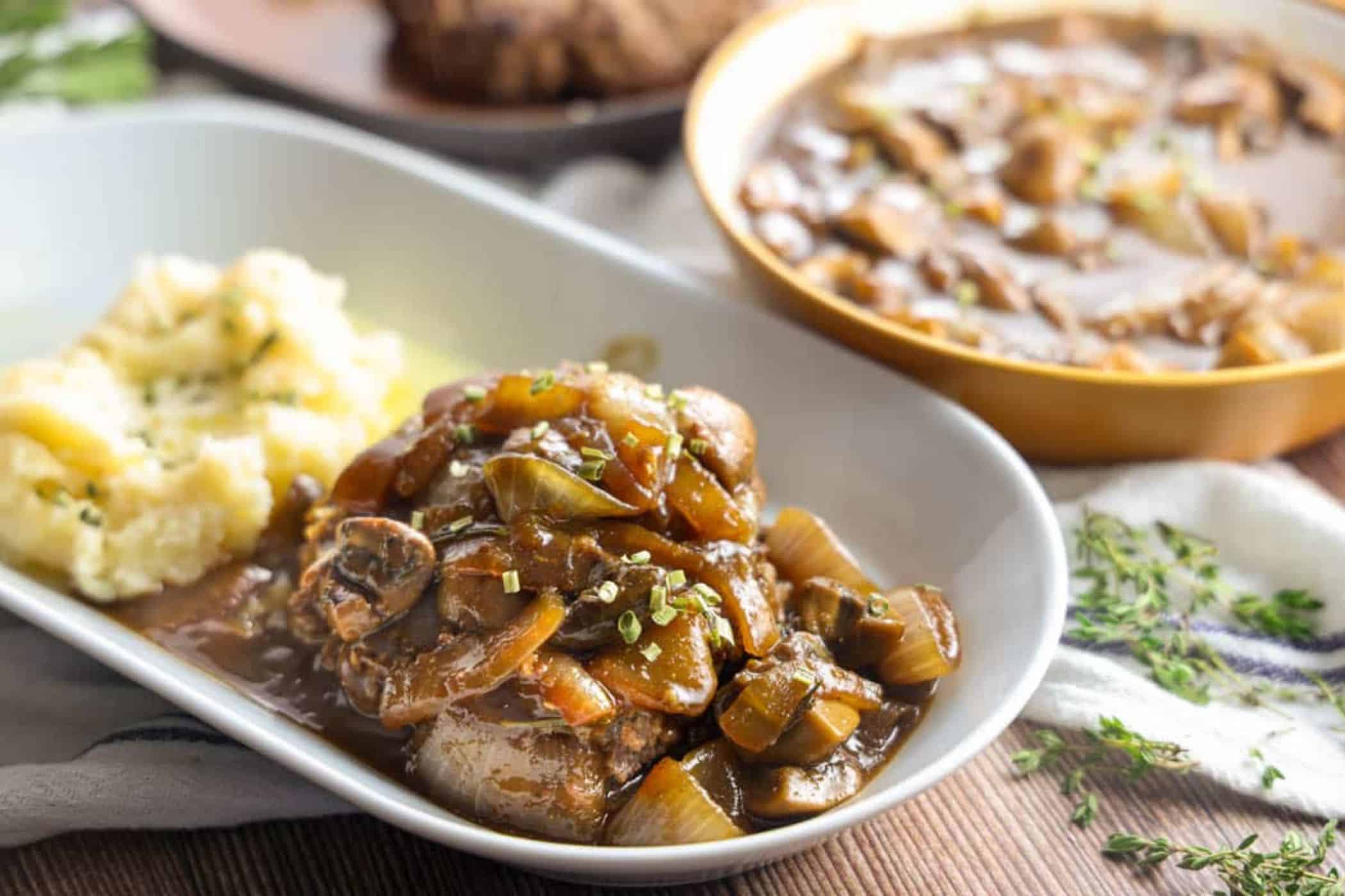 A plate with mashed potatoes and cube steak topped with mushroom and onion gravy—perfect for easy meals or weeknight dinners—with a dish of extra gravy in the background.