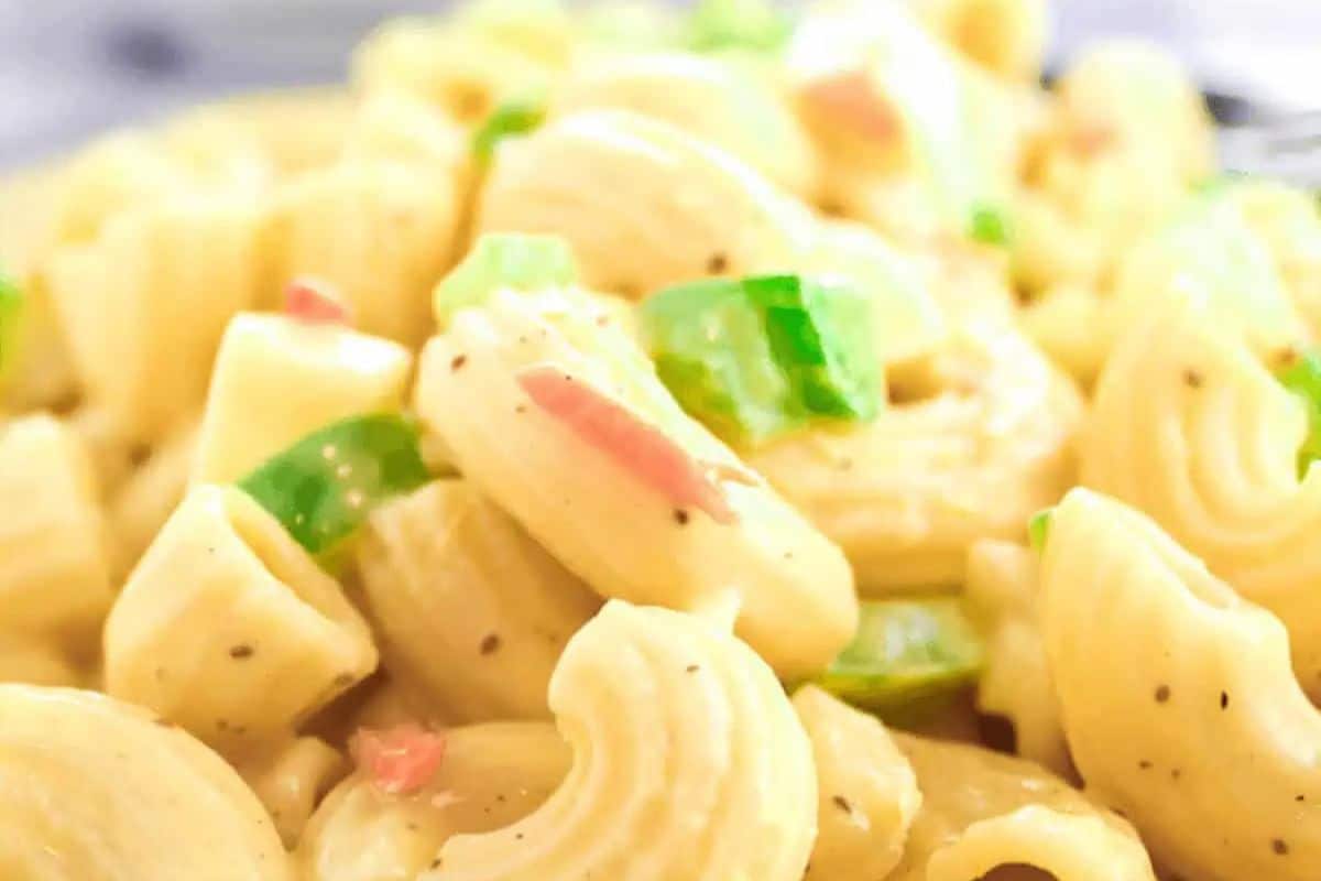 Close-up of cooked macaroni pasta with creamy sauce, diced green bell peppers, and small pieces of red onions, seasoned with black pepper—a nod to classic meals that never go out of style.
