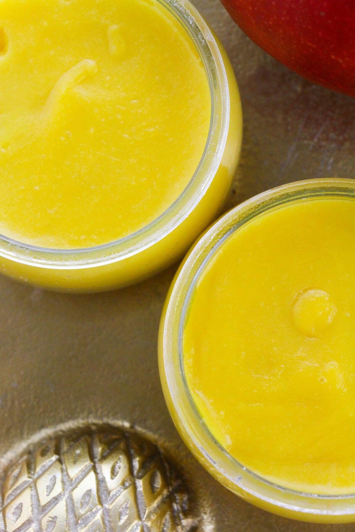 Two small glass jars filled with smooth fruit are placed on a metallic surface next to a decorative object.