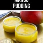 Two small glass jars of creamy Mango Pudding sit on a tray next to a whole mango.