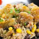 A plate of the meal featuring corn, black beans, shredded chicken, vegetables, and a golden, crispy topping, garnished with chopped parsley.